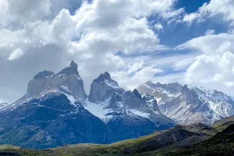 Las cumbres de las Torres del Paine y los picos montañosos circundantes con nieve, bajo un cielo parcialmente nublado. La imagen muestra la majestuosidad del paisaje de la Patagonia chilena, con picos, valles y la distintiva forma de las Torres.