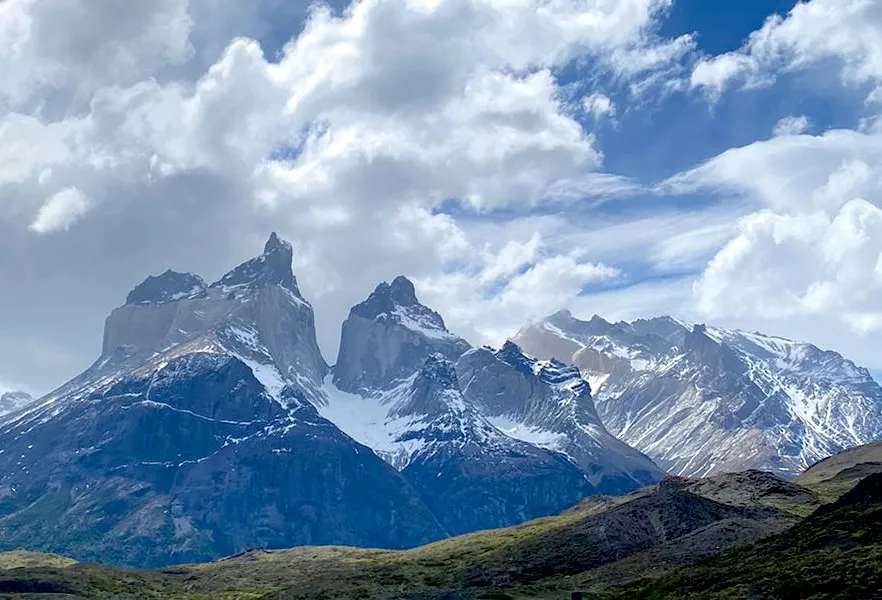 Las cumbres de las Torres del Paine y los picos montañosos circundantes con nieve, bajo un cielo parcialmente nublado. La imagen muestra la majestuosidad del paisaje de la Patagonia chilena, con picos, valles y la distintiva forma de las Torres.