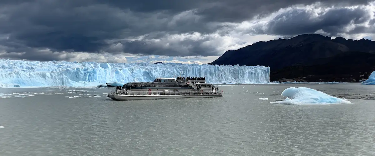 Barco de Safari Azul navegando frente a la pared de hielo del Glaciar Perito Moreno con témpanos flotando